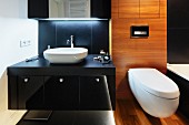 A black washstand next to a wood panelled toilet area