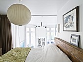 Tagesdecke auf Doppelbett unter Kugellampe im Schlafzimmer, im Hintergrund raumhohe Glasscheibe als Wand