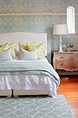 Tapete und Teppich in floralem Pastellblau, kombiniert mit dem zeitlosen Mustermix der Kissen auf einem Bett