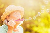 Ältere Frau mit Strohhut bläst Seifenblasen ins spätsommerliche Sonnenlicht