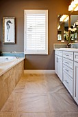 Blick in zeitgenössisches Badezimmer mit Waschtisch, Badewanne, Fliesenboden & Lamellenfenster