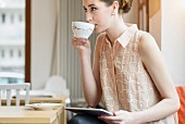 Junge Geschäftsfrau im Café mit Tablet trinkt Kaffee