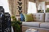 Gemütliches Wohnzimmer mit grauer Couch sowie Zimmerpflanzen, Vasen & Wandbild mit Schmetterlingsmotiv als Dekoration