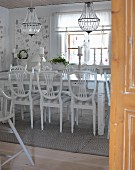 Dining room with white wooden chairs around table below chandeliers with glass ornaments