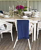 Lit candles on festively set table and white wicker chairs on wooden floor