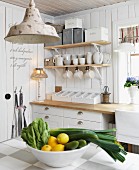 Blick über Schale mit Zitronen und Gemüse auf Küchenzeile, darüber an Wand aufgehängte Konsolen mit weißem Geschirr