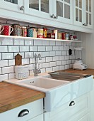 White kitchen counter with ceramic sink and splashback with subway tiles below wall-mounted units