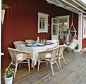 Gedeckter Tisch mit Rattansesseln und Hängestuhl auf der Veranda eines Schwedenhauses
