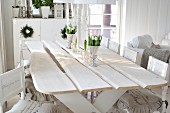 White shabby-chic interior in Scandinavian wooden house with rustic dining table and printed lettering on chair cushions