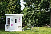 White summer house, table and delicate metal chairs on lawn