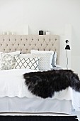 Scatter cushions and fur blanket on double bed with ecru, button-tufted headboard