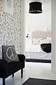 Cushion with CND symbol on black couch against floral, black and white wallpaper outside elegant bedroom with black lampshade