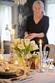 Festlich gedeckter Tisch mit Tischdeko und Kerzenlicht, im Hintergrund Frau