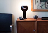 Black, retro table lamp on wooden sideboard next to partially visible, black-covered chair
