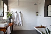 Rustikaler Holztisch mit Aufbauwaschbecken vor Fenster, offene Dusche und Badewanne in weiss gefliestem Bad