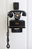 Black vintage telephone mounted on white wooden wall