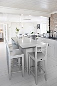 Pale grey bar stools at free-standing counter in open-plan kitchen with white wooden floor