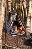 Woman and man lying in makeshift tent looking at autumn woods; vintage ambiance