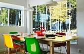 Colourful shell chairs around wooden table in corner; view of woodland through panoramic window