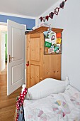 Bed with white wooden frame in front of farmhouse wardrobe in child's bedroom