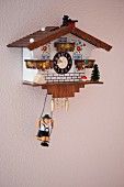 Cuckoo clock with small figurine on swing suspended beneath on pink-painted wall