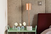 Glass vases and table lamp with copper-coloured lampshade on side table painted pastel green