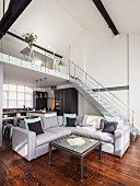 Coffee table and grey corner sofa in open-plan, loft-style interior with staircase leading to gallery in background