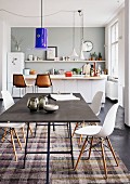 Blue Murano glass lampshade above black table and Eames Plastic Chairs in front of kitchen counter