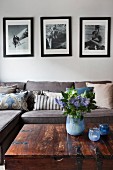 Retro black and white photos above sofa with collection of scatter cushions; vase of flowers and tealight holders in shades of blue on trunk table