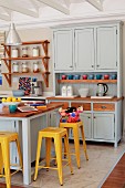 Yellow vintage bar stools at counter in pastel grey Shaker-style kitchen