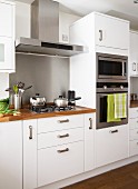 Gas hob with extractor hood and separate oven and microwave in white, fitted kitchen with wooden work surfaces