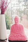 Pink Buddha statue next to white vase of red twigs on windowsill