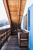 Wooden balcony of restored Swiss chalet with sky-blue shutters and view of snowy mountain landscape