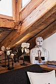 Collection of artistic papier mâché flowers and modern bust on L-shaped shelf under sloping ceiling with dormer window
