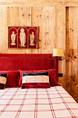 Religiöses Triptychon über dem rot gepolsterten Kopfteil eines Doppelbetts; Wände aus massivem Naturholz