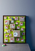 Hand-crafted Advent calendar with small parcels attached to picture frame with green background leaning against wall