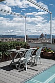 Seating area with vintage metal chairs painted white and weathered wooden table on roof terrace with view across Florence
