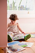 Kleines Mädchen sitzt auf Zimmerboden und betrachtet Bilderbücher