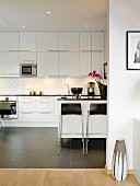 White, modern fitted kitchen with tiled floor, worksurface and bar stools in contrasting black
