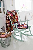 A colourful, crocheted patchwork blanket on a rocking chair next to a side table with an espresso jug