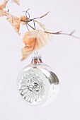 Silver Christmas bauble hanging from birch twig with dry leaves