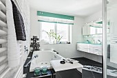 Modernes, schwarz-weisses Badezimmer mit Whirlwanne, davor verchromte Box als Hocker und Wäschebehälter, im Hintergrund Waschtisch für Zwe