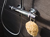 A natural sponge hanging on a shower tap mounted on brown, marbled wall tiles