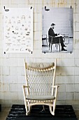 Rocking chair with white-painted wooden frame on wooden pallet below posters taped on unrendered sand-line brick wall