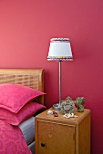 Bedside cabinet with lamp against raspberry wall next to Art Nouveau bed with cane headboard and pink bed linen