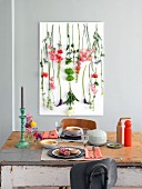 Flowers hanging from a picture hung on a pale grey wall with a table laid for two in front of it