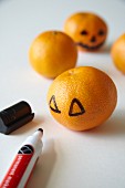 Drawing spooky Jack-o'-lantern faces on tangerines for Halloween
