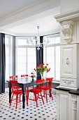 Black wooden table and red wooden chairs on black and white tiled floor in elegant window bay