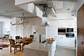 White, open-plan kitchen with free-standing island counter and ceiling lamp made from branch above traditional dining set
