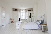 Grosses Schlafzimmer mit skandinavischem Vintage-Charme; alter Küchenhocker als Nachtisch, im Hintergrund Fenster flankiert von Einbauschränken